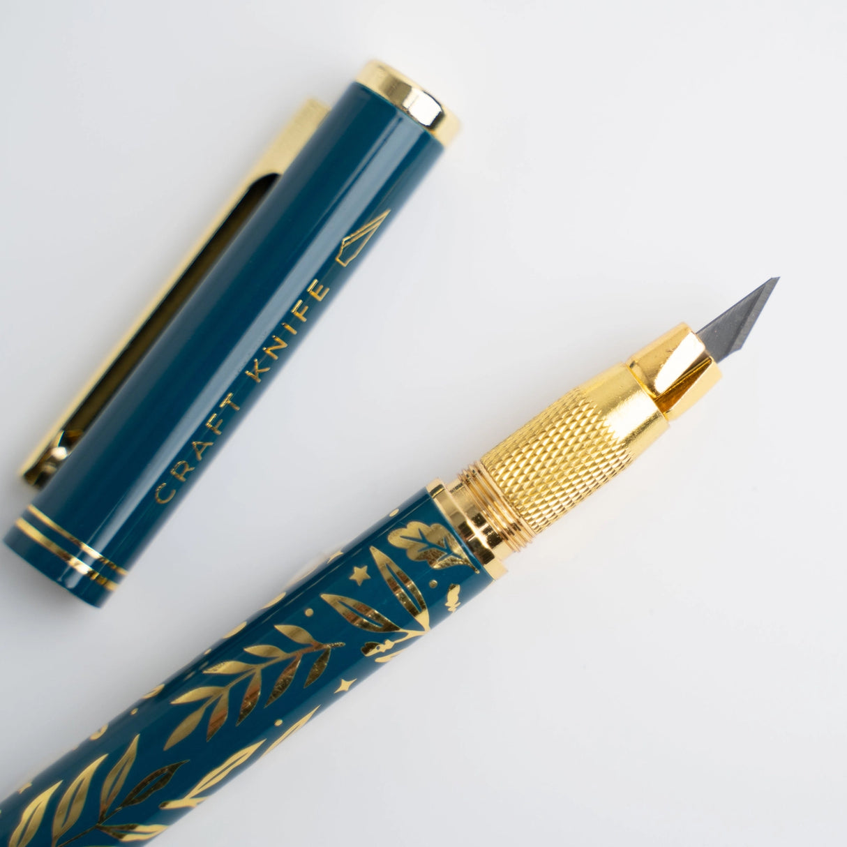 A beautifully designed craft knife featuring a deep teal barrel adorned with gold botanical detailing. With its precision blade and sturdy metal construction, this tool brings both function and elegance to journaling, scrapbooking, and detailed paper crafting.
Specs & Details:
Material: Metal body with gold accents
Design Theme: Teal barrel with gold botanical illustration
Blade: Precision craft blade (replaceable)
Features: Removable cap for safe storage, textured grip for control
Use: Ideal for cutt