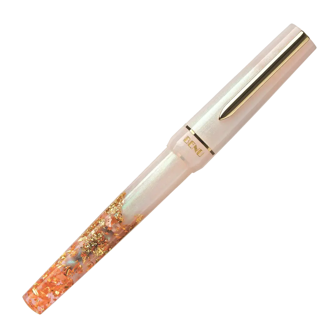 BENU presents the newest Haute Collection — a line of elegant, fashion-inspired pens that blend classic charm with bold, modern flair. The designs include both subtle and vibrant styles, showcasing BENU’s signature glitter and color artistry. Each pen features a faceted body with alternating wide and slender facets, complemented by either gold-plated or chrome-plated trims for a sleek, timeless look.
A mix of golden flakes dances through a soft, pearly pink base, complemented by gleaming gold trim. Tender