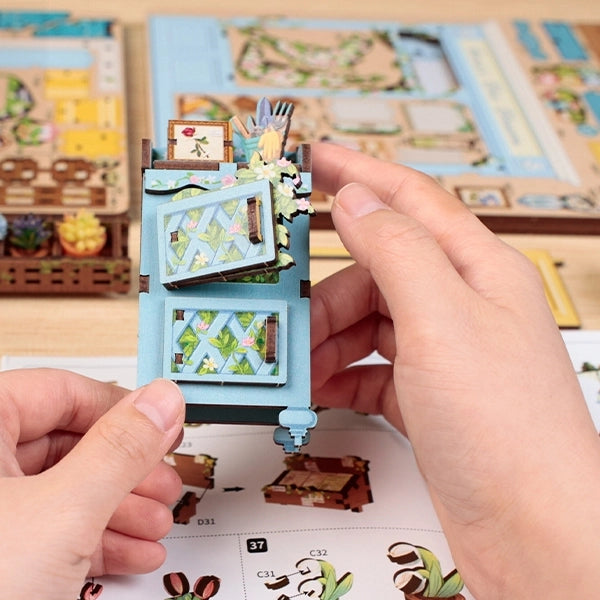 Step into the charm of a quaint flower shop with the Anna's Blue Blossom DIY Miniature Book Nook Kit. From the soft pastel storefront to the cheerful yellow door and overflowing baskets of vibrant blooms, every detail captures the essence of a dreamy neighborhood florist. Inside, shelves brim with blossoms, potted plants, and tiny gardening treasures, creating a warm and welcoming scene. The delicate floral canopy and cascading greenery add a fresh touch of life, making this kit feel like a stroll through a