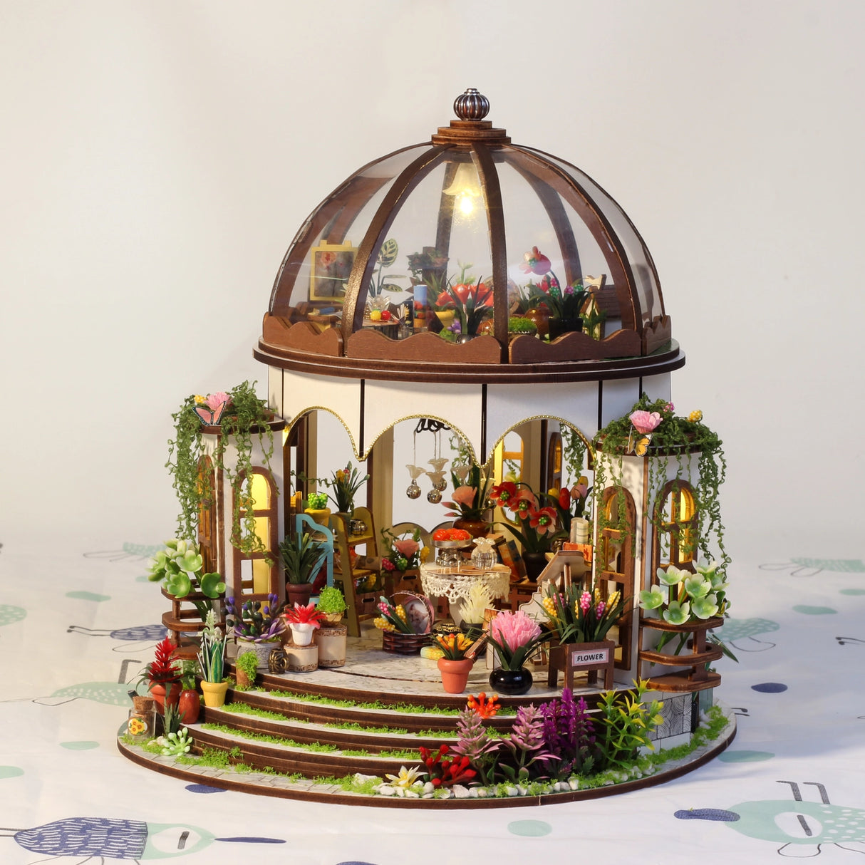 Step into a tranquil garden escape with this miniature kit-a sun-drenched sanctuary filled with flourishing plants, rustic charm, and peaceful vibes. This beautifully crafted greenhouse-style gazebo features delicate woodwork, glass-like panels, and an inviting open-air design surrounded by vibrant flowers, climbing vines, and cozy garden furniture. Whether you're dreaming of a relaxing afternoon under the sun or a quiet place to sip tea and tend to your plants, this miniature brings that dream to life-one
