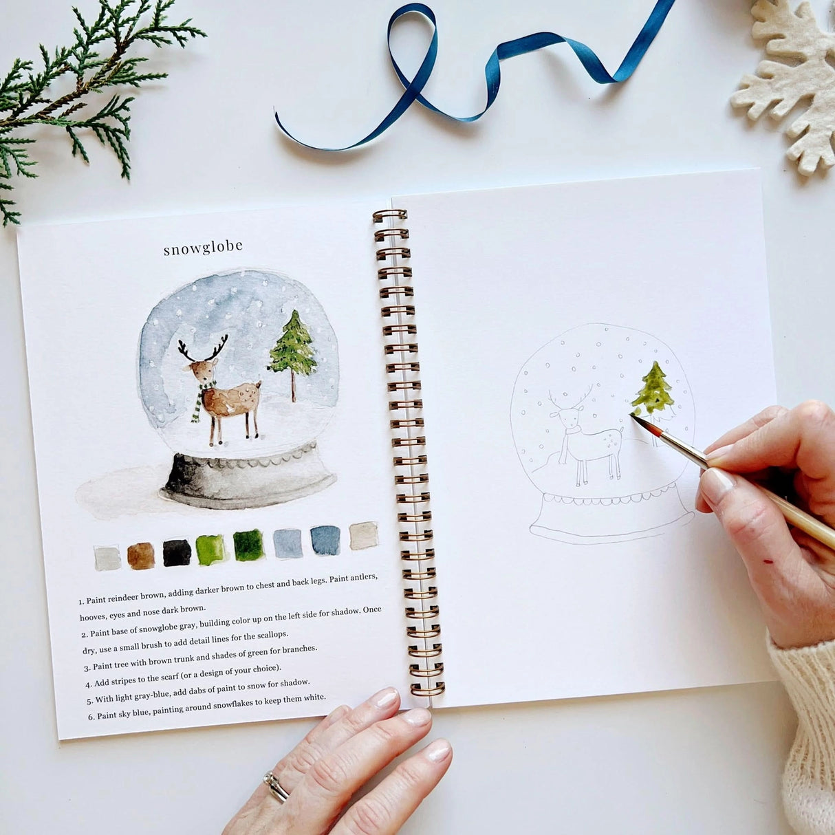 Twelve winter illustrations — a snowman, A-frame cabin, fair isle sweater, snow globe, ice skaters, mittens, and more — each pre-outlined with step-by-step instructions. Paintings take about thirty minutes from start to finish, making it approachable for first-time painters and a favorite for gifting.