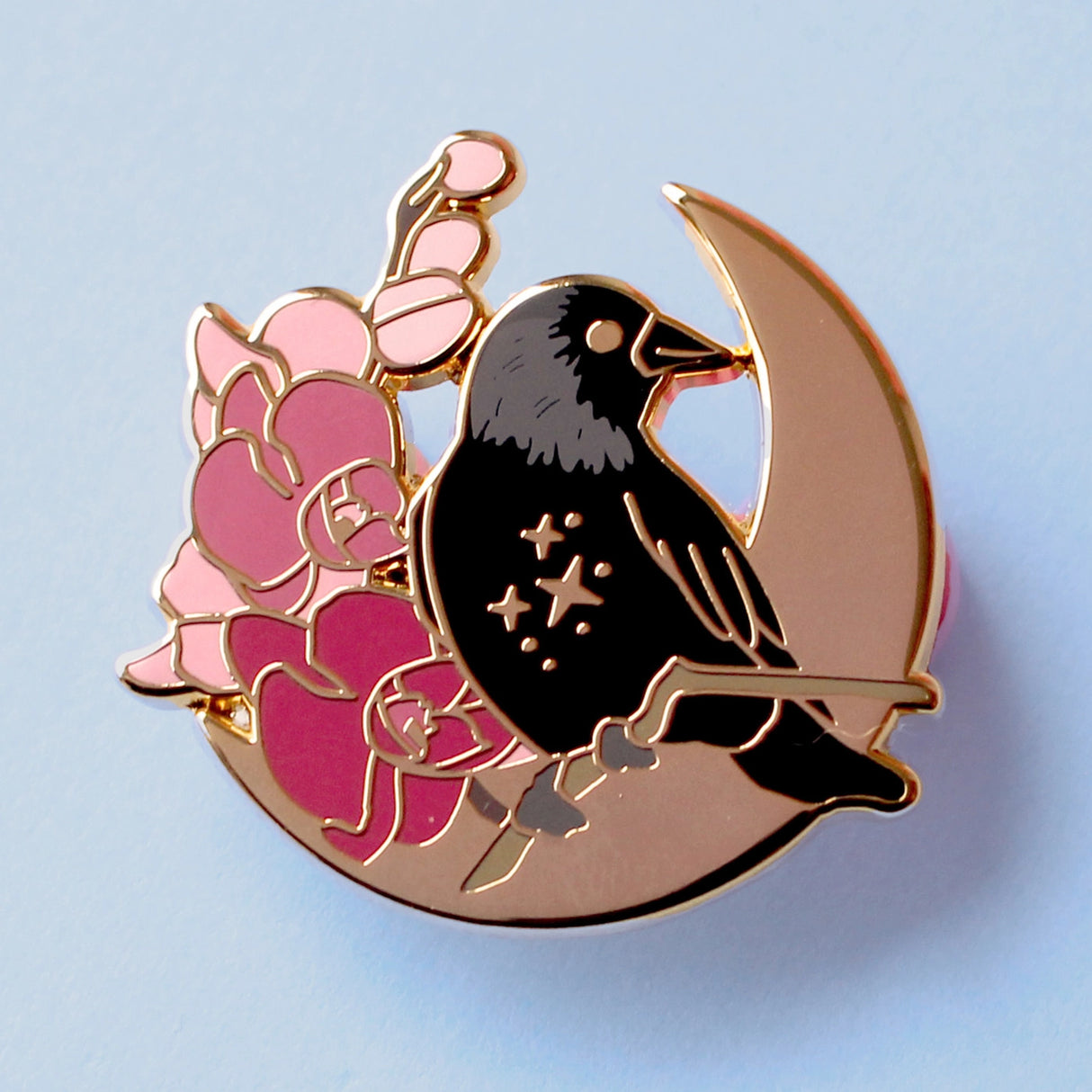 This enamel pin features a Jackdaw perching on a branch of pink orchid flowers, in front of a large gold moon. The pin is presented on a Glitter Punk backing card and is secured with 2 pin backs.
This pin is part of the Corvid Collection, an 8-part series of bird pins.
Measurements: 35mm
