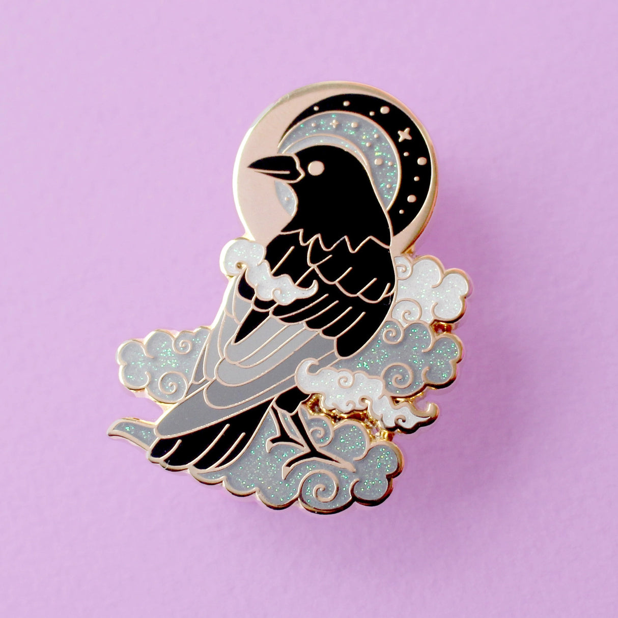 This enamel pin features a black crow surrounded by grey glittery clouds, and a starry moon with grey backgrounds. The pin is presented on a Glitter Punk backing card and is secured with 2 pin backs.
This pin is part of the Corvid Collection, an 8-part series of bird pins.
Measurements: 39mm