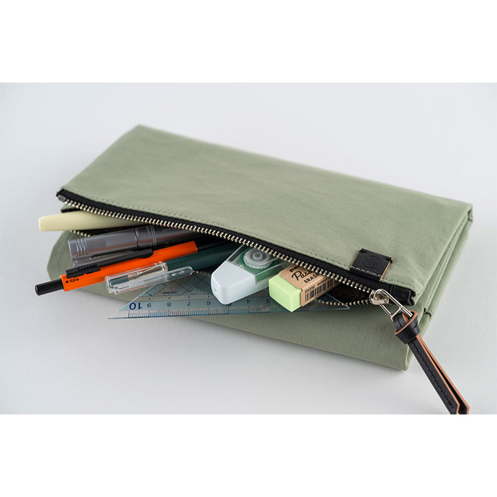 Its standout feature is the generously sized pocket, but its overall appearance remains clean and minimal. With its calming and gentle oakmoss color, the design is versatile and suits anyone. Though it folds into thirds and fastens with a magnetic closure, the cover is light in hand. The aim was effortless elegance, something that looks sharp without being flashy. The material is a soft nylon with a sophisticated sheen.