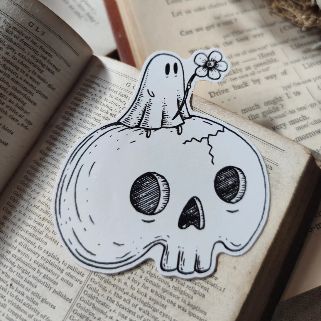 A little ghostie with a flower, perched atop a spooky skull, on a die-cut vinyl sticker. From original ink artwork by Jon Turner.