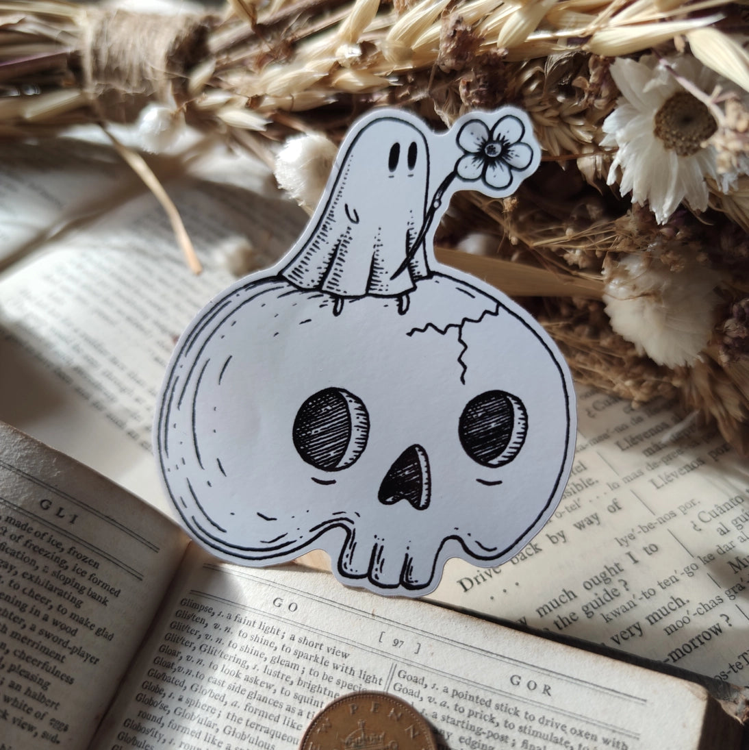A little ghostie with a flower, perched atop a spooky skull, on a die-cut vinyl sticker. From original ink artwork by Jon Turner.