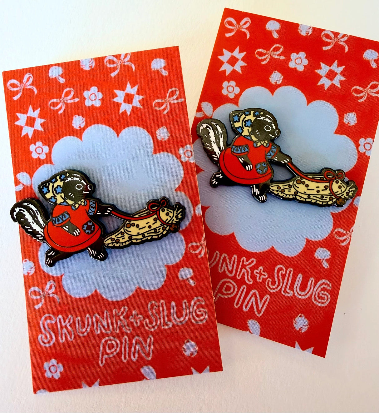 A Skunk and their friend the Slug take a walk through the forest.
This hard enamel pin measures approximately 1.75" and features a rubber clasp for easy closure and two back posts so pin stays where you stick it. Comes with a back card.