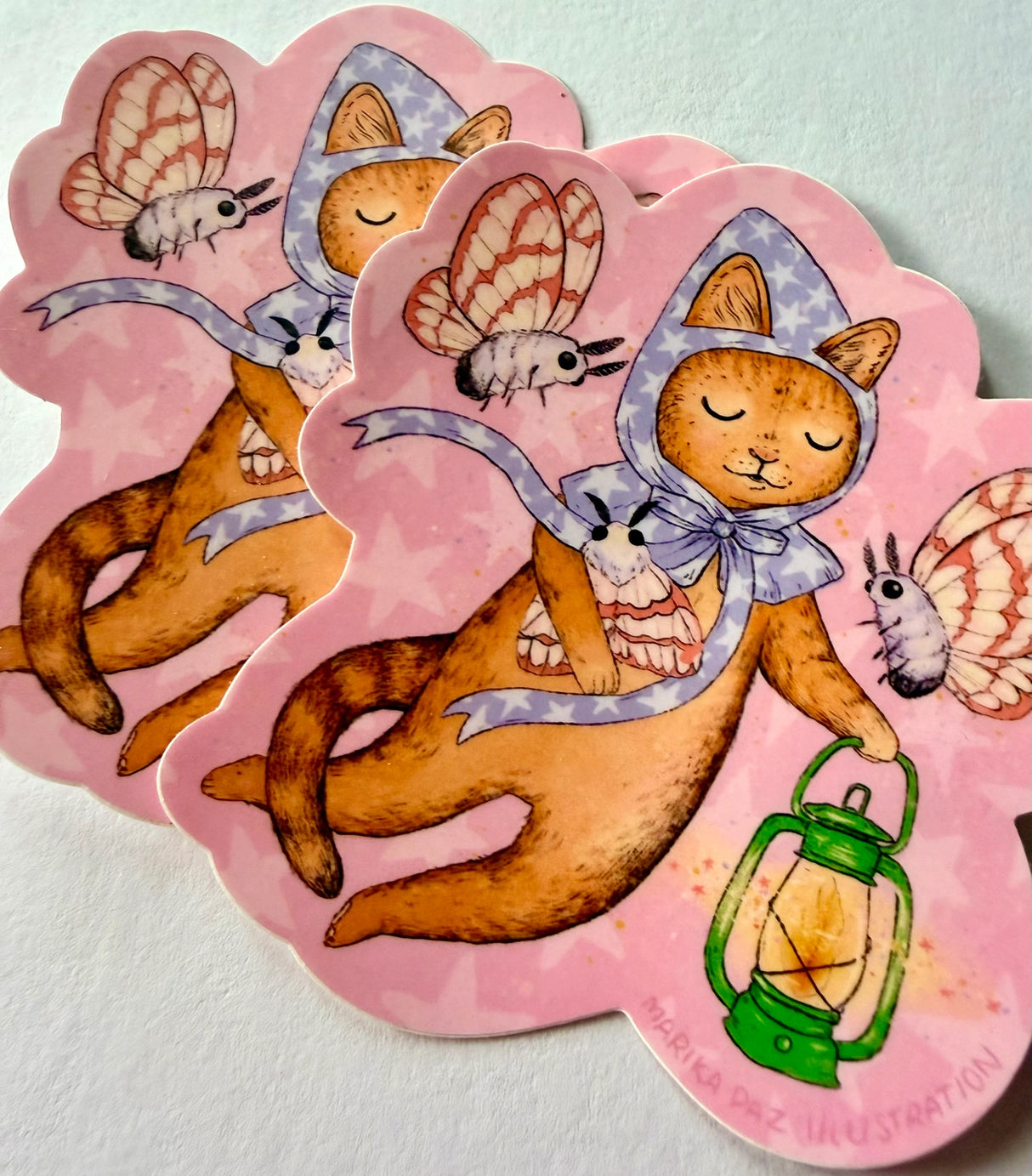 A cat and his lantern attract moths as they float amongst the stars.
This vinyl matte sticker is weather and waterproof-stick it on a notebook, bike, or car- it's going to stick around! Heck, throw it on a water bottle and through the dishwasher. This sticker can go anywhere. Sticker measures 3.5" x 4.5" Printed in USA.