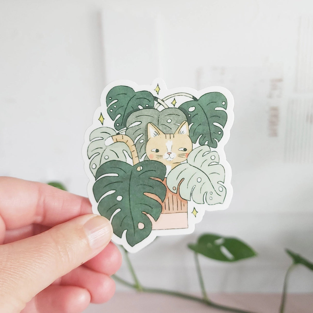 A curious cat settles among lush monstera leaves, tucked into the calm greenery of a Wildflower Woods cottage. This vinyl sticker captures that cozy, plant-filled moment, bringing a touch of quiet charm to your everyday essentials.
Made from durable, waterproof vinyl, this sticker is designed to hold up wherever you place it—whether that’s a water bottle, laptop, or journal you reach for daily.