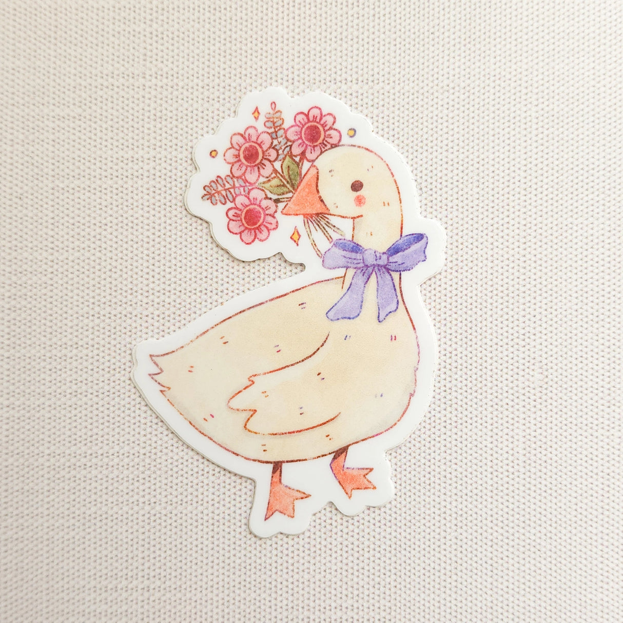 A sweet goose pauses with a bouquet of flowers held gently in its beak, a blue bow tied neatly at its neck. This vinyl sticker captures that charming, flower-filled moment, adding a warm, cottage-inspired touch to your everyday essentials.
Made from durable, waterproof vinyl, this sticker is designed to hold up wherever you place it—whether that’s a water bottle, laptop, or journal you reach for daily.