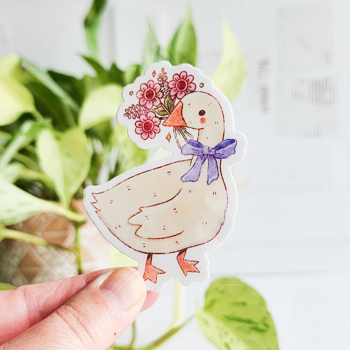 A sweet goose pauses with a bouquet of flowers held gently in its beak, a blue bow tied neatly at its neck. This vinyl sticker captures that charming, flower-filled moment, adding a warm, cottage-inspired touch to your everyday essentials.
Made from durable, waterproof vinyl, this sticker is designed to hold up wherever you place it—whether that’s a water bottle, laptop, or journal you reach for daily.