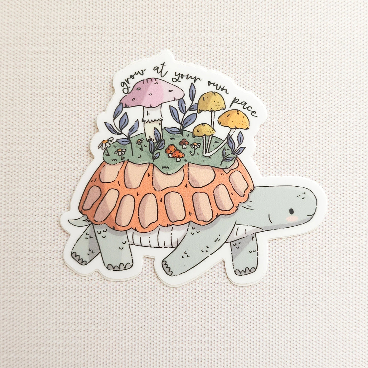 A turtle travels along a mossy path in Wildflower Woods, carrying a tiny mushroom meadow on its back as it moves steadily forward. This vinyl sticker captures that unhurried moment, carrying a gentle reminder that growth happens in its own time.
Made from durable, waterproof vinyl, this sticker is designed to hold up wherever you place it—whether that’s a water bottle, laptop, or journal you reach for daily.