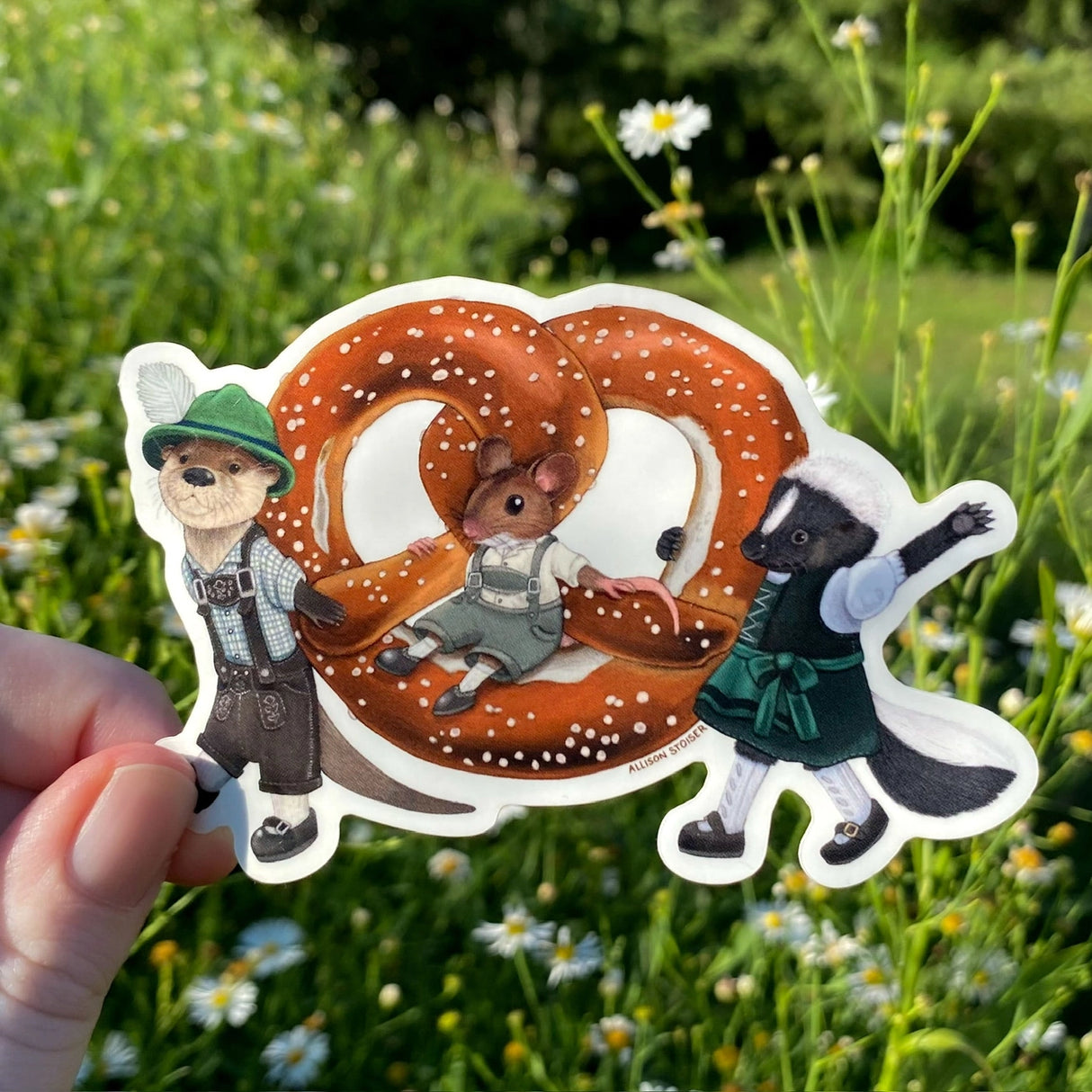 These critters are ready for Oktoberfest! Dressed in their finest lederhosen and dirndl, this otter and skunk are proudly carrying a larger-than-life pretzel. Their mouse pal is just along for the ride!
This die-cut gloss vinyl sticker is durable, weatherproof, and perfect for water bottles, notebooks, laptops, bikes, and all sorts of other surfaces! Make sure to clean and dry the surface thoroughly before applying.