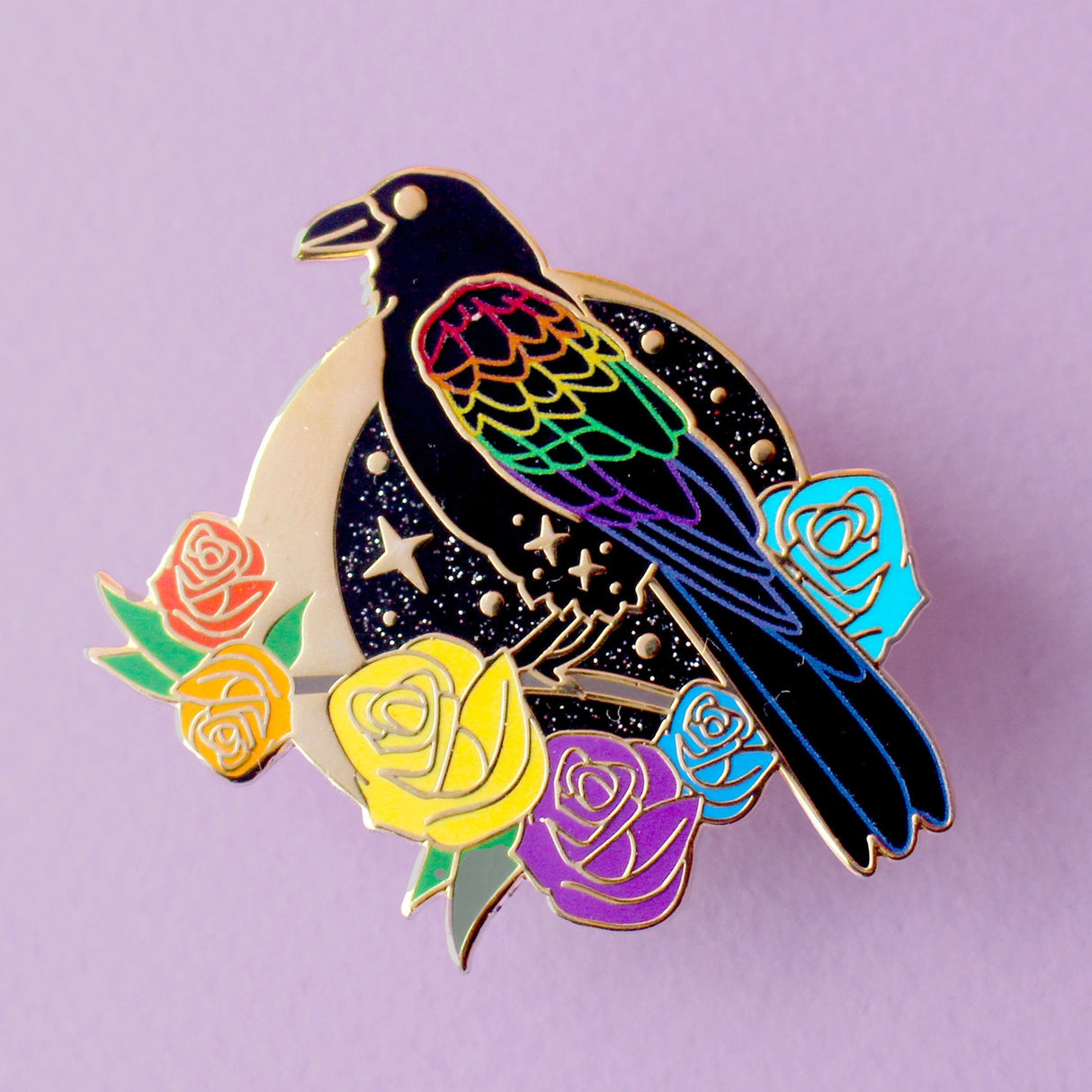 This enamel pin features a black raven with rainbow-coloured wings. It’s sitting on a branch surrounded by rainbow-coloured roses, in front of a glittery moon. The pin is presented on a Glitter Punk backing card and is secured with 2 pin backs.
This pin is part of the Corvid Collection, an 8-part series of bird pins.
Measurements: 42mm