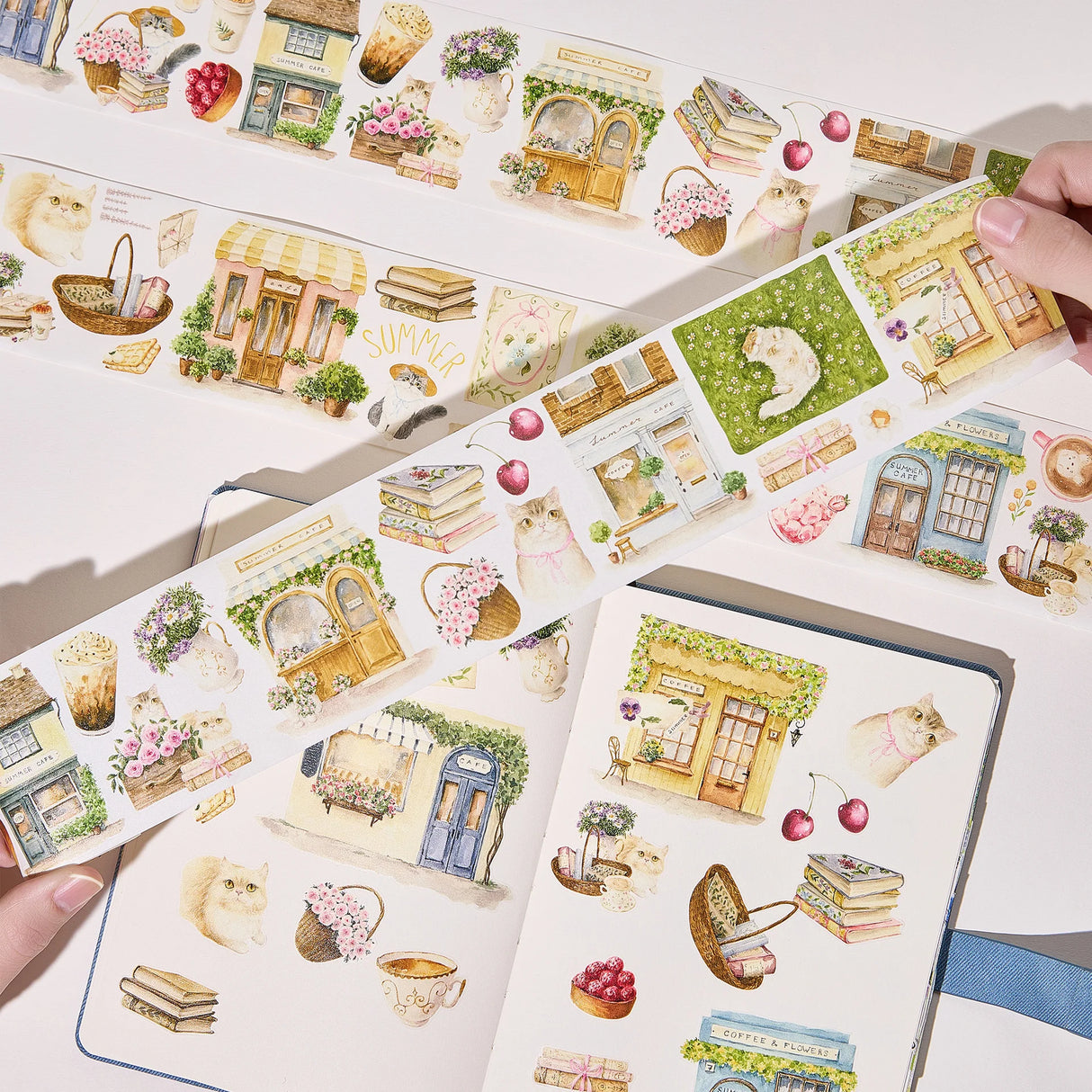 Step into a world where nature and comfort collide. Our Summer Café Wide Tape transforms your stationery into a bustling garden bistro, teeming with life, blooming flowers, and the true owners of the cafe: the cats.
This whimsical design weaves together the architecture of charming coffee shops with the wild beauty of summer florals. Nestled among the potted plants and open doors, you’ll find hand-painted cats exploring, sleeping, and playing. 