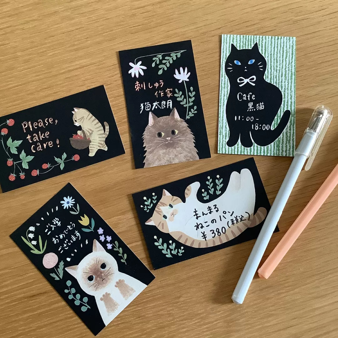 Set of cat-themed cards on a wooden surface with a pen.