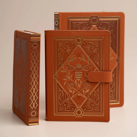 Let your creativity buzz with warmth and intention. The Keeper of the Bees Notebook in Rust blends golden honeybee symbolism with rich, earthy tones, creating a journal that feels both enchanting and grounding. Perfect for capturing ideas, documenting your days, or exploring your imagination—this notebook turns every page into a moment of magic.