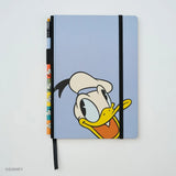 This medium notebook includes 160 pages of 100GSM blank paper and a matte hardcover featuring Donald Duck and Daisy Duck. It also has a built-in pencil holster that comes loaded with a Donald Duck Blackwing pencil.