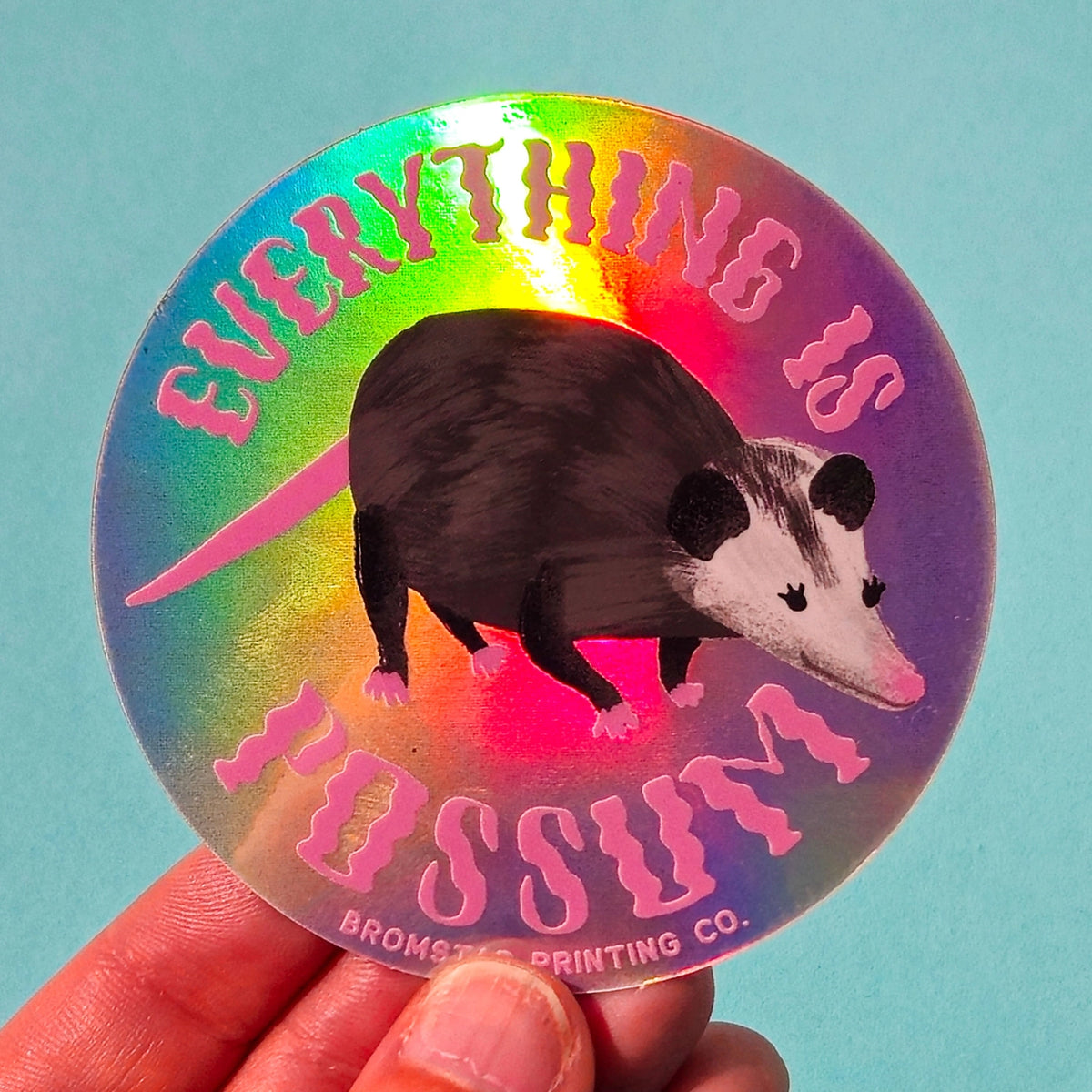 For the person who loves Tegan and Sara AND possums! Everything is awesome with this trippy holographic sticker featuring a charming possum illustration and the words "Everything is Possum." This 3" holograph sticker is ideal for adorning water bottles, laptops, and more.