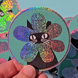 Product description
A black cat with a clipped ear wears a sparkly flower around their face. Truly, the rarest bloom. This 3" super sparkly glitter sticker is purrfect for adorning water bottles, laptops, and more. Watch how it catches the light!