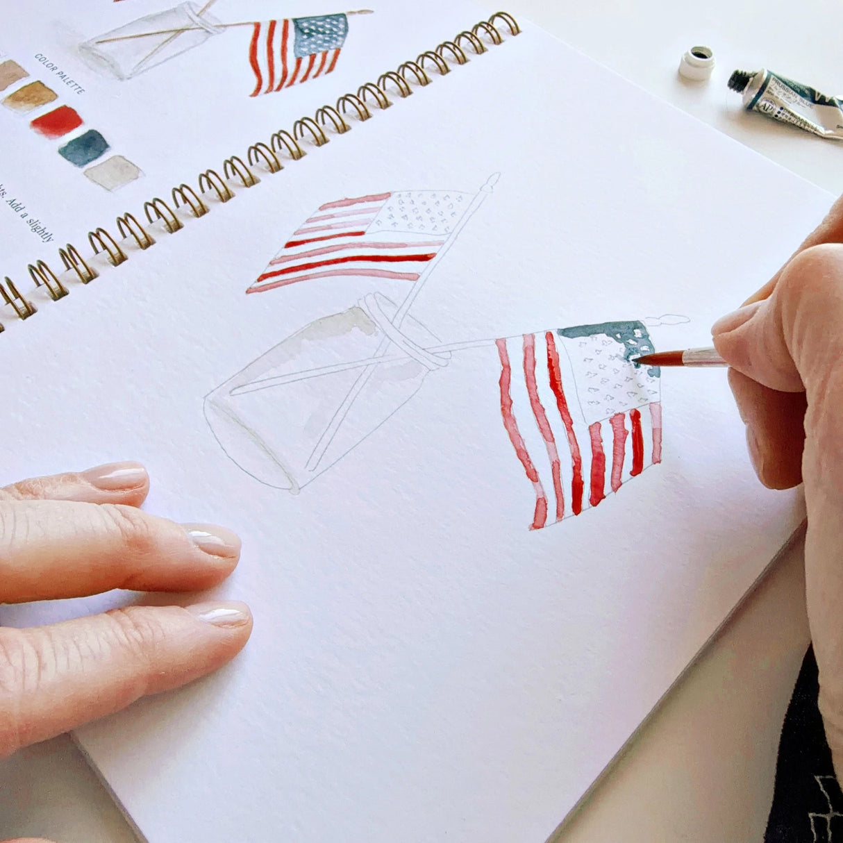 Twelve illustrations of flags, stars, and classic summer scenes — each pre-outlined with step-by-step instructions. Paintings take about thirty minutes from start to finish, making it approachable for first-time painters and a favorite for gifting.

A timely release for America's 250th anniversary in 2026. A strong May–July seller and a natural fit for home, gift, and patriotic-themed boutiques.

12 beginner-friendly illustrations
Thick 120lb watercolor paper&nbsp;
Lay-flat pages with spiral binding for has