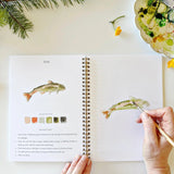 Twelve camping illustrations — a vintage camper, lantern, campfire, tent, canoe, s'mores, and more — each pre-outlined with step-by-step instructions. Paintings take about thirty minutes from start to finish, making it approachable for first-time painters and a favorite for gifting.