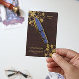 Carry the Sakura Street Estie beyond the page with this oversized hard enamel lapel pin. The 7.5 cm gold- plated design recreates the fountain pen with a sparkle effect inspired by its translucent purple material. It brings one of the collaboration's central designs to jackets, bags, and pin collections.