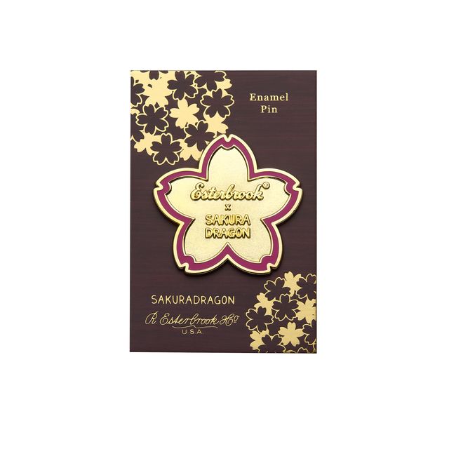 Inspired by the blossoms found throughout Cindy Duong's Sakura Street illustrations, this oversized hard enamel pin features a sakura flower outlined in gold-plated metal. The 5 cm design includes Esterbrook and Sakuradragon branding at its center, creating a collectible emblem of the collaboration.