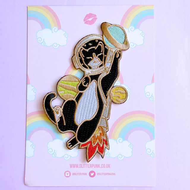 This awesome Astronaut Cat patch features a tuxedo cat with a helmet and rocket ship playing with some planets.

Beautifully woven with multi coloured threads, this fabulous patch with brighten up any coat, bag or hat!

Measurements: 64mm x 110mm