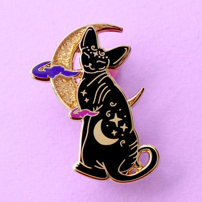 Cute, cuddly and clever – there’s no cat quite like a Sphynx! This fab enamel pin features a black Sphynx covered in mystical symbols, sitting in front of a crescent moon with 2 purple clouds.

The pin is 42mm (1.65”) tall, and is made from gunmetal hard enamel, with glitter and UV printed details. It's secured with 2 pink clutches to keep the pin in place.