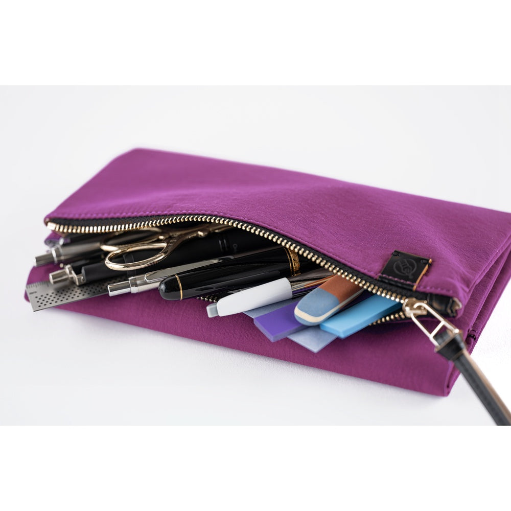 Its standout feature is the generously sized pocket, but its overall appearance remains clean and minimal. The aim was effortless elegance, something that looks sharp without being flashy. Adding a subtle pop is the reddish-purple color. It’s eye-catching yet refined, with a mature tone. Though it folds into thirds and fastens with a magnetic closure, the cover is light in hand. The material is a soft nylon with a sophisticated sheen.
