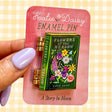 A tiny treasure for book lovers, wildflower wanderers, and collectors of small beautiful things.
This interactive enamel pin features a working hinge that allows the miniature book to open and close, revealing a hidden floral spread inside. Inspired by beloved vintage books and meadow blooms, it’s a little story you can wear on your jacket, tote, sweater, or favorite old flannel.

Details:
• 1.75” on the longest side
• Interactive hinged design that opens like a tiny book
• Gold-plated finish
• Rich, detail