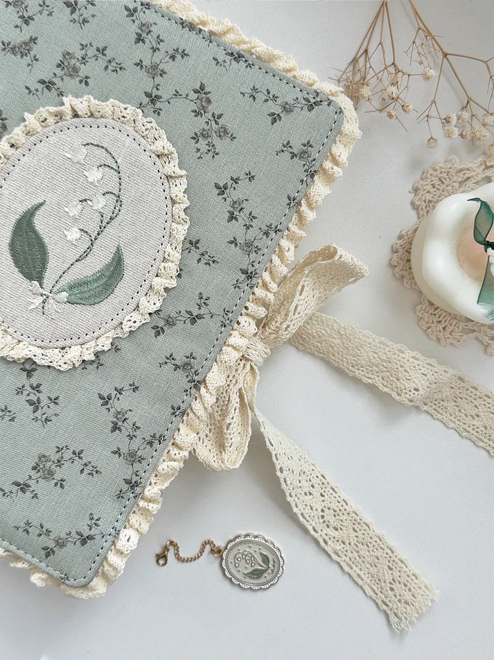 lily&nbsp;of the valley fabric notebook cover. sewn together with careful craftsmanship. lined with lace ruffles for that extra romantic, cottage-core, fairytale touch. meant to protect your notebooks &amp; a keepsake for your beloved stationery :)

♡ floral linen pattern with ruffle lace edging &amp; lily of the valley embroidery

♡ lace ribbon enclosure to help keep your notebooks closed

♡ 7 pockets total (left sleeve: 5 pockets | right sleeve: 2 pockets)

♡ x1 lace ribbon book mark with gold bow pendant