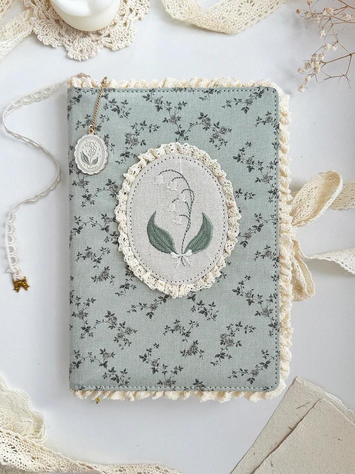 lily&nbsp;of the valley fabric notebook cover. sewn together with careful craftsmanship. lined with lace ruffles for that extra romantic, cottage-core, fairytale touch. meant to protect your notebooks &amp; a keepsake for your beloved stationery :)

♡ floral linen pattern with ruffle lace edging &amp; lily of the valley embroidery

♡ lace ribbon enclosure to help keep your notebooks closed

♡ 7 pockets total (left sleeve: 5 pockets | right sleeve: 2 pockets)

♡ x1 lace ribbon book mark with gold bow pendant