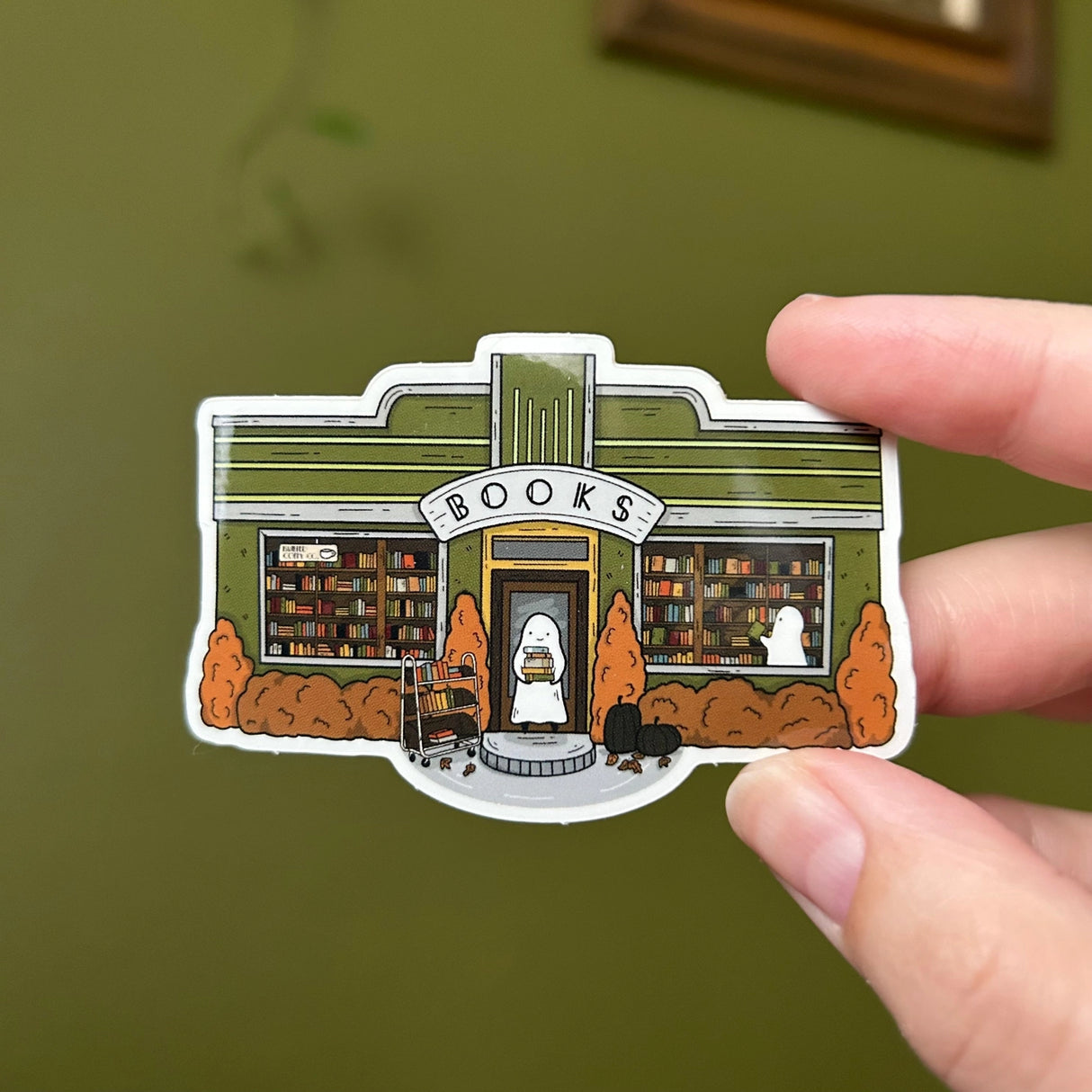 Glossy sticker of a little art deco bookshop where a ghost with a stack of books stands in the doorway.

3in wide
Waterproof
Glossy finish