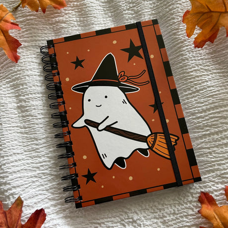 A new A5 notebook featuring a ghost dressing up as a witch!

This hardcover notebook comes lined and with an elastic band. There are 96 double sided pages.