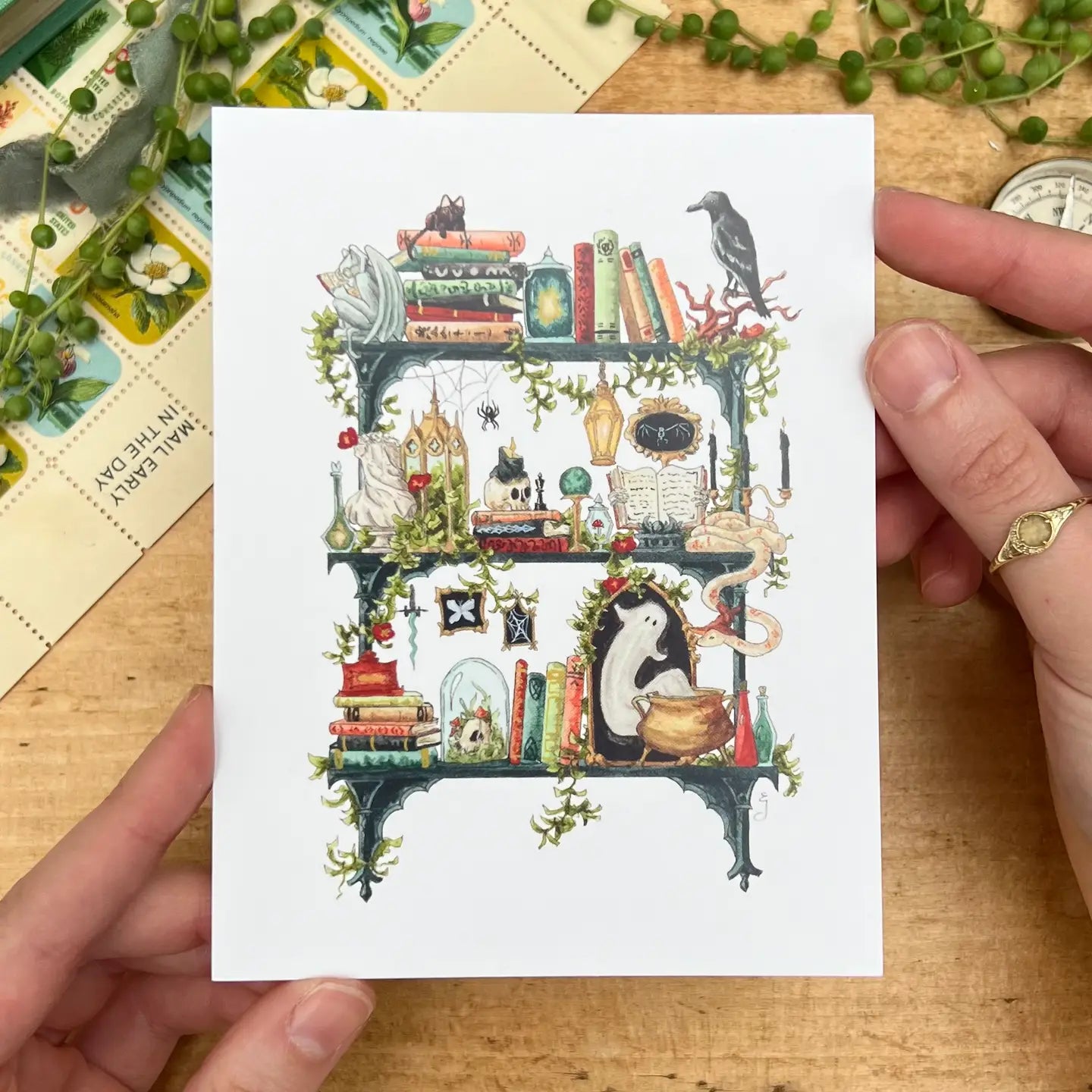 Postcard featuring my original watercolor and ink illustration of the oddities, spooky creatures, and enchanting books tucked away on the shelves of a gothic witch, including a gargoyle enjoying a book, a snake chatting with a spider, and a mysterious ghost.