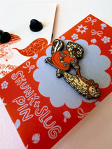 A Skunk and their friend the Slug take a walk through the forest.

This hard enamel pin measures approximately 1.75" and features a rubber clasp for easy closure and two back posts so pin stays where you stick it. Comes with a back card.