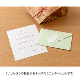 The set shows a rabbit stretching and chasing a strawberry. The stationery paper is a soft pink color inspired by strawberries. The ruled lines are designed to evoke the image of a rabbit bouncing around.