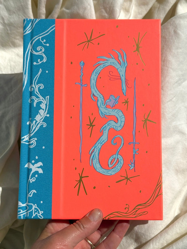 This is a blank 200 page notebook/sketchbook with thin ivory Munken paper perfect for light sketching or writing. Part of a fantasy collection called Woodfolk.

The cover is fluorescent pink/orange and has a smooth matte finish with gold foiling on the front and back. Plus it has a blue fabric spine with white embossing, adding to the charm of the book. Best for pencils, light pens, and generally light mediums, as thick markers or water can bleed. Not recommended for gouache or heavy marker use.
