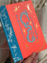 This is a blank 200 page notebook/sketchbook with thin ivory Munken paper perfect for light sketching or writing. Part of a fantasy collection called Woodfolk.

The cover is fluorescent pink/orange and has a smooth matte finish with gold foiling on the front and back. Plus it has a blue fabric spine with white embossing, adding to the charm of the book. Best for pencils, light pens, and generally light mediums, as thick markers or water can bleed. Not recommended for gouache or heavy marker use.