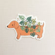 A charming dachshund planter rests among leafy greenery, a thriving cheese plant growing from its back like a small piece of playful décor. This vinyl sticker captures that cozy, plant-filled still life, adding a touch of warmth and whimsy to your everyday essentials.

Made from durable, waterproof vinyl, this sticker is designed to hold up wherever you place it—whether that’s a water bottle, laptop, or journal you reach for daily.