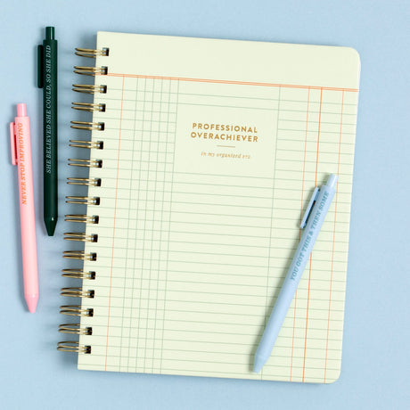 The Professional Overachiever Spiral Notebook is here for your color-coded lists, carefully planned goals, and every brilliant idea in between. With a vintage ledger-inspired cover, gold foil lettering, and 160 lined pages, this 7x9” notebook is your go-to for planning, journaling, or conquering your to-do list. The sturdy spiral binding and double-sided pocket keep everything organized—just how you like it. Perfect for students, teachers, planners, and anyone proudly in their “organized era.” Makes a thoug