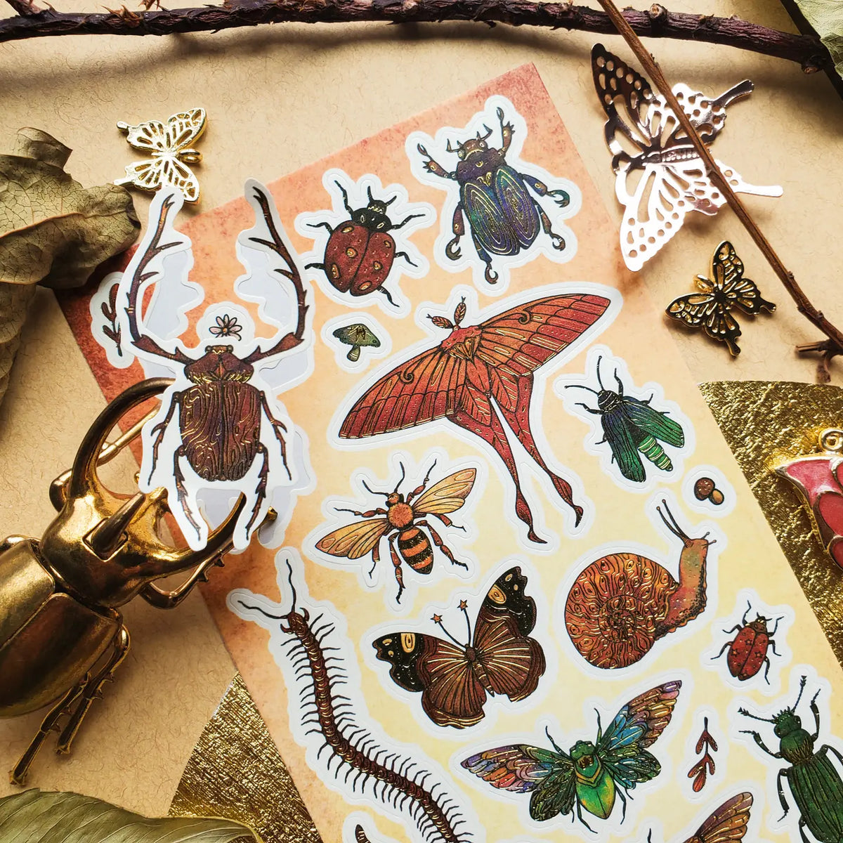 🪲🦋 Bugs get the grand treatment in this striking collection of richly detailed beetles, moths, butterflies, cicadas, and other curious crawlers! Dressed in jewel-toned greens, fiery reds, burnished golds, and intricate patterns, these tiny creatures prove that the insect world can be every bit as bold and beautiful as it is wonderfully wild.

One sticker sheet is included.

• Top Coating: Gold foil
• Adhesive Layer: Paper
• Backing Layer: Paper
• 6.69" x 3.54"
• Weight: 0.03 oz