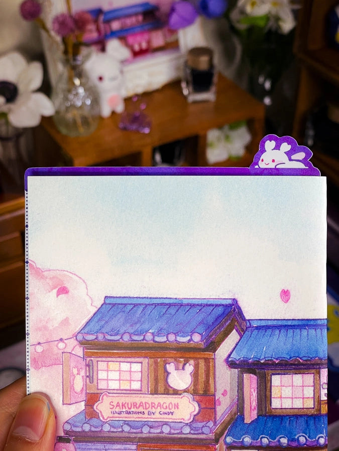 Sakuradragon - Sakura Street A6 Pencil Board

A napping Sakuradragon perched onto of a cozy little shop Sakura Street. It's almost as if she is sleeping on top of your notebook.

What is a pencil board?
Pencil boards are inserts for your notebook that sit under the page you are writing on. They prevent indents on the next page when you write and even prevent ink from bleeding through to the page beneath. But honestly, they can just be cute bookmarks.