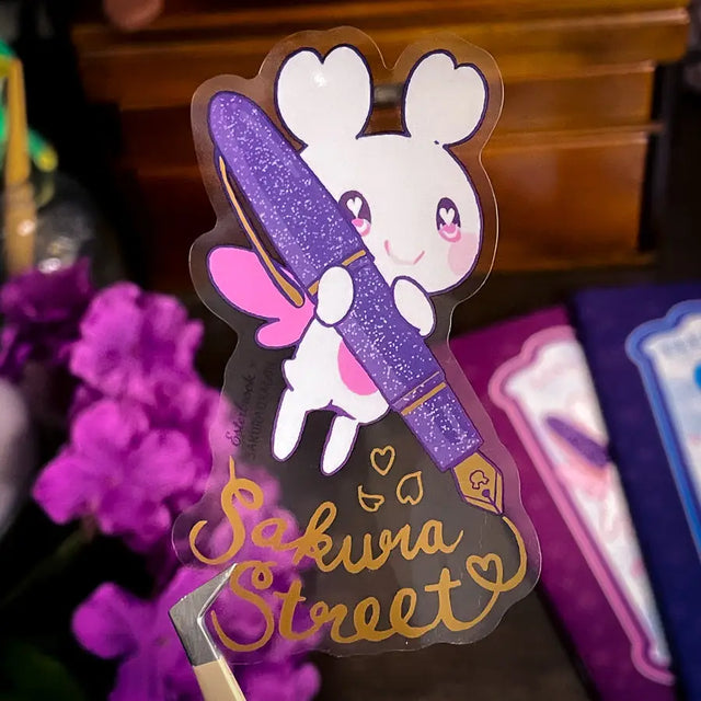 Sakuradragon - Sakura Street Fountain Pen Clear Vinyl Sticker

Sakuradragon really look like she's shining with that pen.

Product Details:

• Material: PET (clear plastic - oil proof, UV resistant, and waterproof)
• Dimensions: 3.5in x 2.37in
• Foil: Gold
