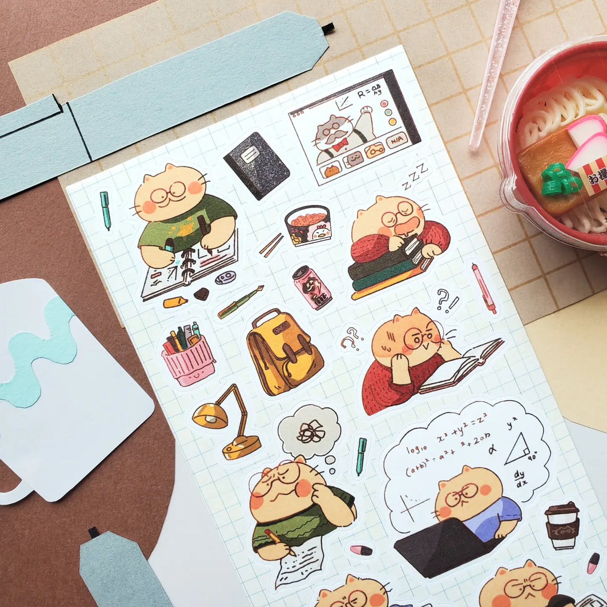 @chaioverdose’s hardworking kitty knows that studying is a full-time adventure! Between tackling tricky equations, filling notebooks with notes, attending online classes, and squeezing in a quick nap on a stack of books, there’s always something to keep those paws busy. Luckily, a little instant ramen and plenty of coffee are here to help this studious cat power through!

Art by: @chaioverdose
One sticker sheet is included.
Top Coating: None
Adhesive Layer: Paper
Backing Layer: Paper
Size: 6.69"x3.54"
