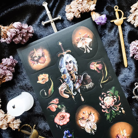In @iratxe.yc’s shadowed garden, nothing is quite as it first appears. Jeweled flowers gaze back from curling stems, delicate moths wear watchful eyes, and a silver-haired guardian stands adorned in blossoms, gemstones, and armor. Rich with surreal beauty and dark botanical magic, this striking sheet reveals a forest where every petal may be hiding a secret.

Art by: @iratxe.yc

One sticker sheet is included.
Top Coating: None
Adhesive Layer: Paper
Backing Layer: Clear PET
Size:6.69"x3.54"
Weight-0.03oz