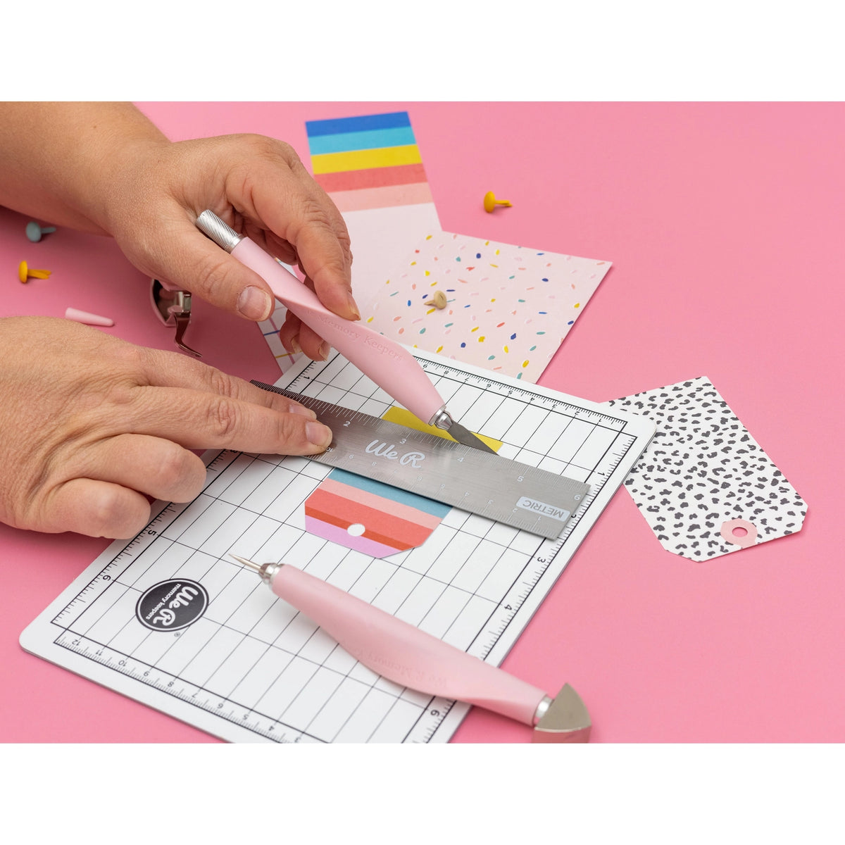 The We R Makers Mini Tool Kit in Pink is the ultimate companion for all your DIY craft projects. This comprehensive kit includes essential tools: a cutting mat, ruler, scissors, craft knife, tweezers, brad setter, and piercing tool. Designed for versatility, it's perfect for scrapbooking, journaling, card making, and a wide range of other crafts.

The vibrant pink color adds a fun and stylish touch to your toolkit, while the high-quality construction ensures each tool is durable and reliable. The cutting ma