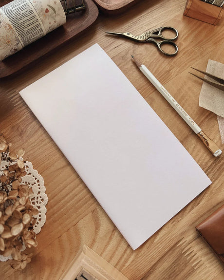 Sarica Studio Cream Notebook (Standard TN Size) White sheet of paper on a wooden surface with stationery items.